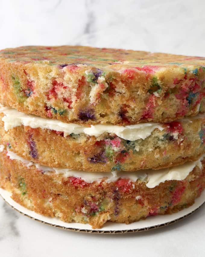 three layers of funfetti cake sitting on a round piece of cardboard with white icing between them