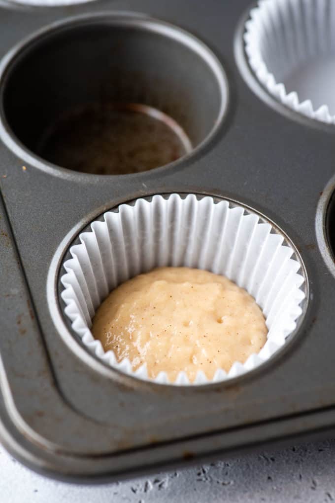 a muffin pan with a white muffin liner in the corner spot and some muffin batter in the bottom of it