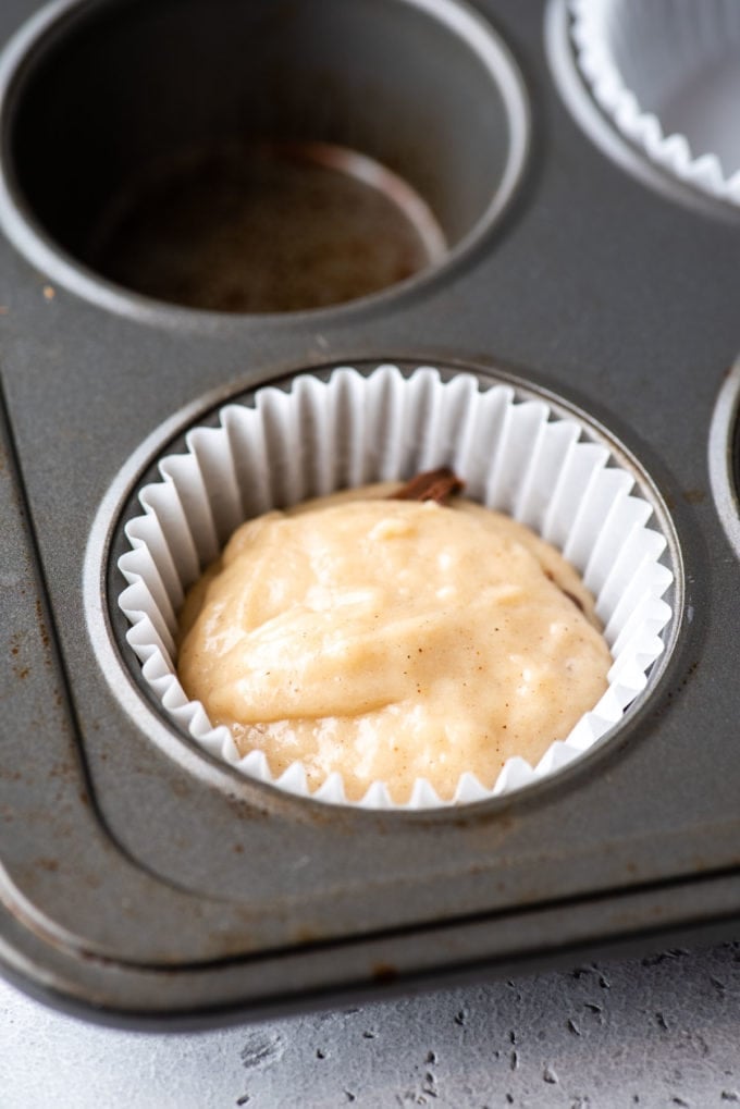 a muffin pan with a white muffin liner in the corner spot and some muffin batter in the bottom of it and layers of muffin batter and nutella inside the liner