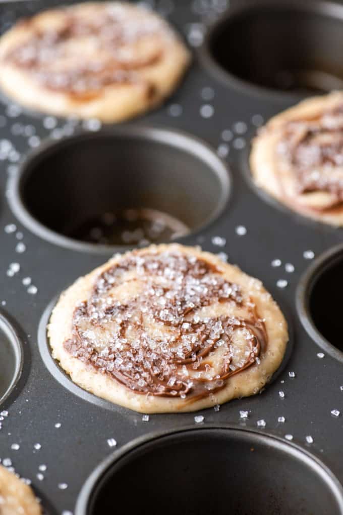 a muffin pan with the batter for nutella swirl muffins in every other muffin hole, topped with sanding sugar