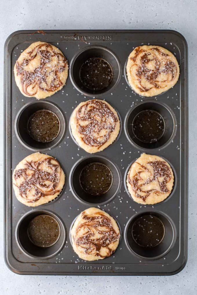 a muffin pan with nutella swirl muffin batter in every other hole with sanding sugar on top