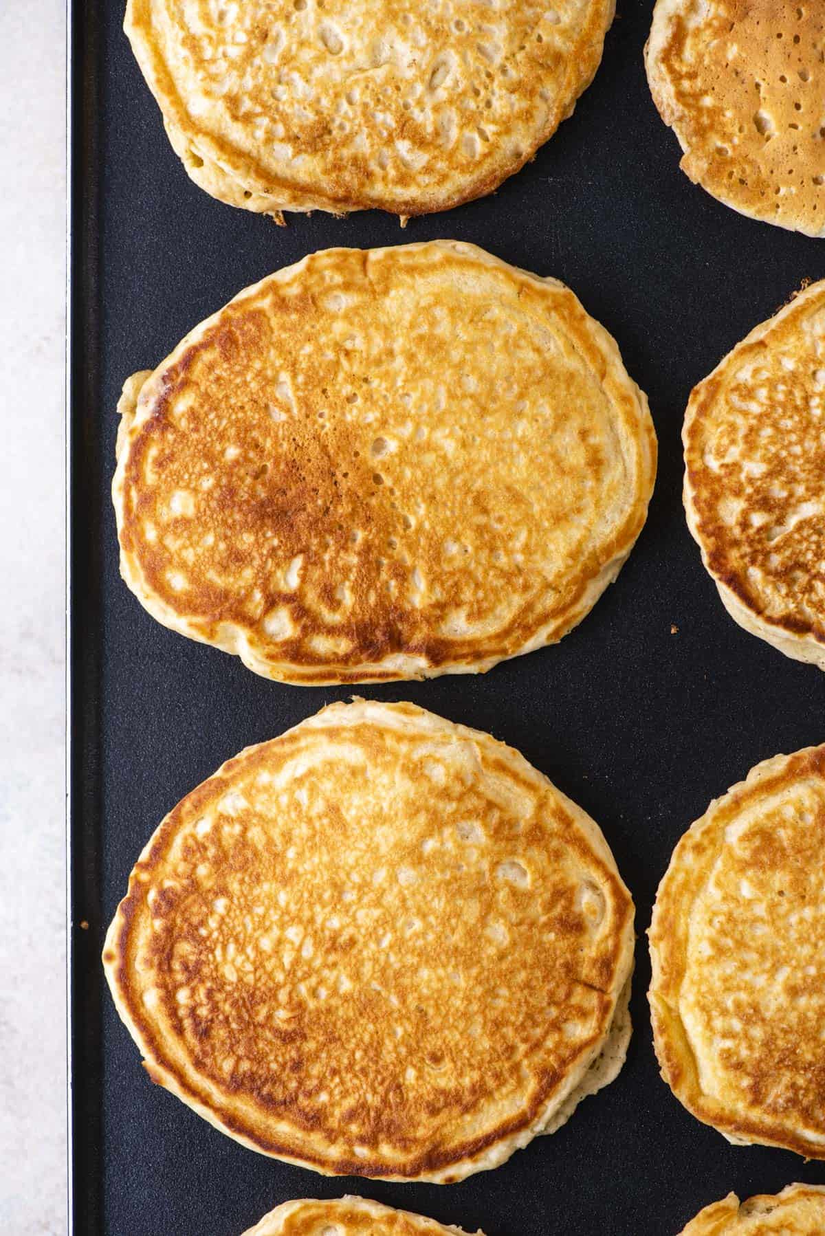 rows of golden brown pancakes cooking on a griddle