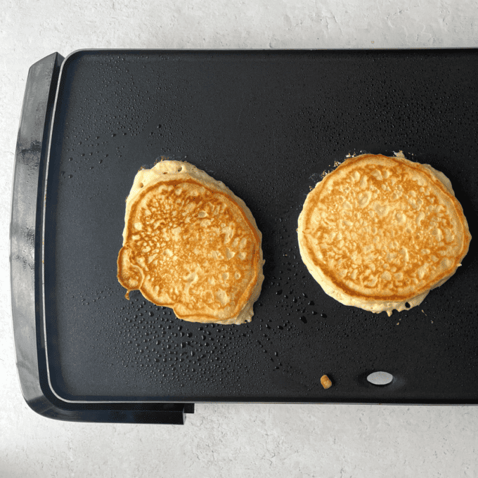 two pancakes being cooked on a flat-top griddle