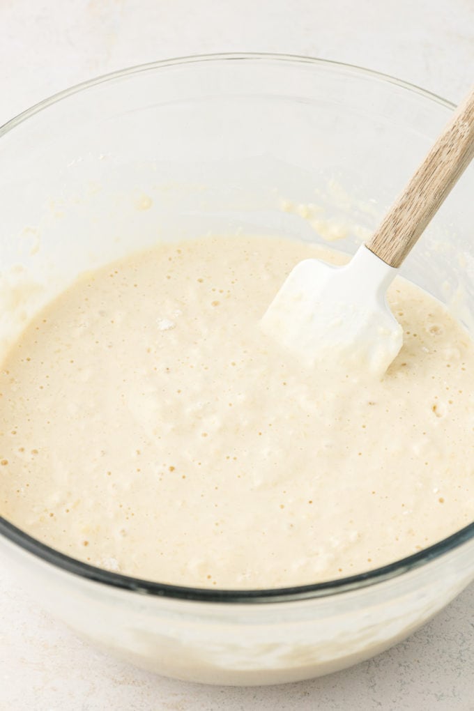 sheet pan pancake batter in a clear glass bowl on a white surface with a spatula leaning inside the bowl