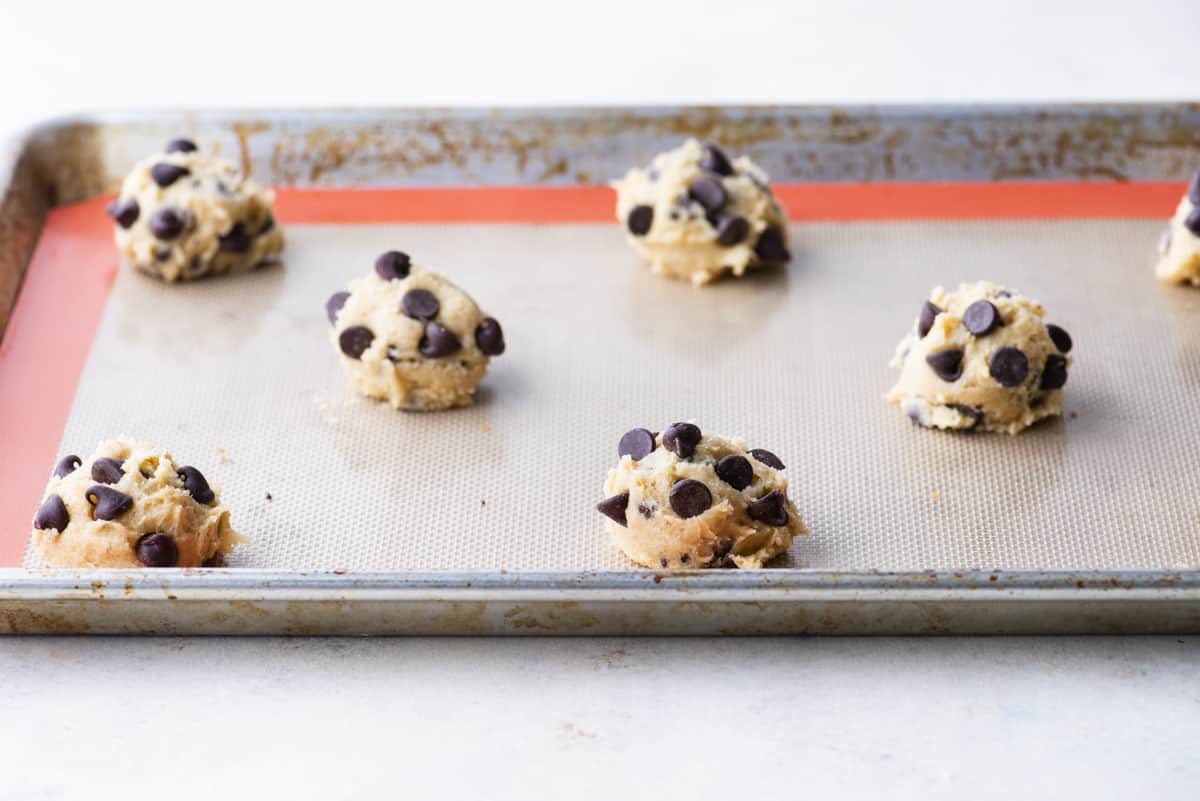 balls of toll house chocolate chip cookie dough spaced out on a baking sheet covered in a nonstick liner