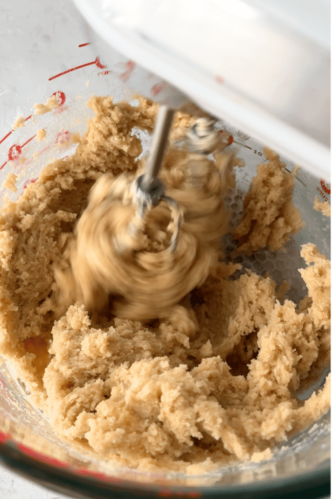 butter, brown sugar and sugar being mixed by an electric mixer in a measuring bowl