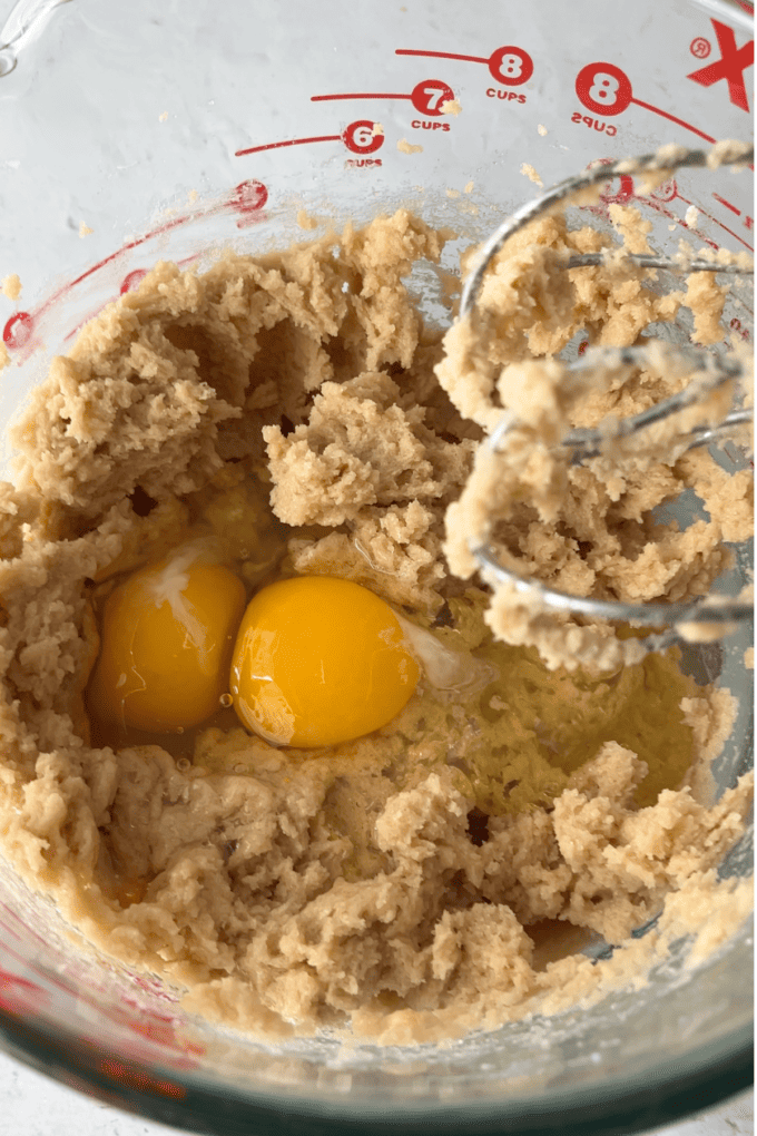 a butter and brown sugar mixture with two eggs on top inside a clear glass pyrex measuring bowl with beater/mixers leaning on the side
