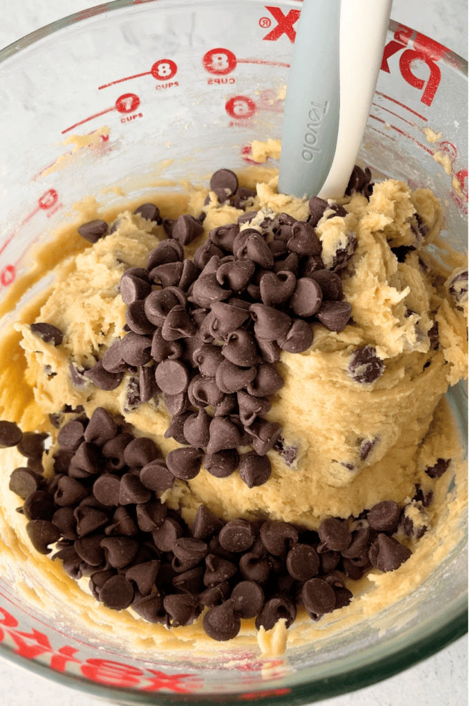 batter for toll house cookies in a clear glass measuring bowl with chocolate chips on top