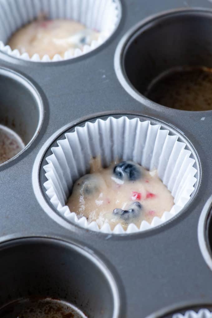 triple berry cheesecake muffin batter in the bottom of a muffin liner in a muffin pan