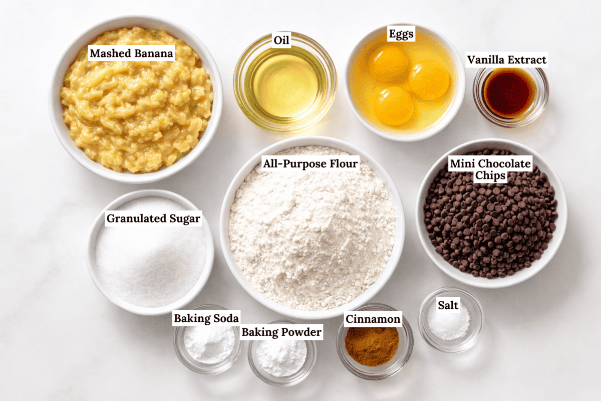Bowls of mashed banana, oil, eggs, vanilla extract, all-purpose flour, mini chocolate chips, granulated sugar, baking soda, baking powder, cinnamon, and salt are arranged on a white surface&mdash;perfect for banana chocolate chip muffins.