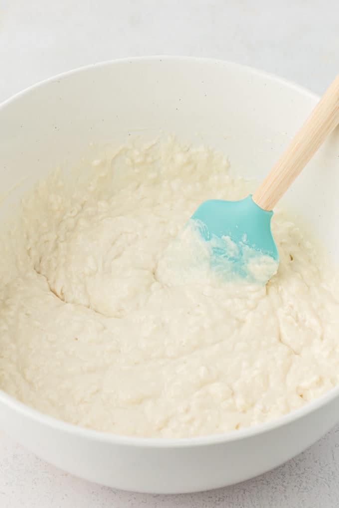 buttermilk pancake batter being stired in a white bowl with a teal spatula