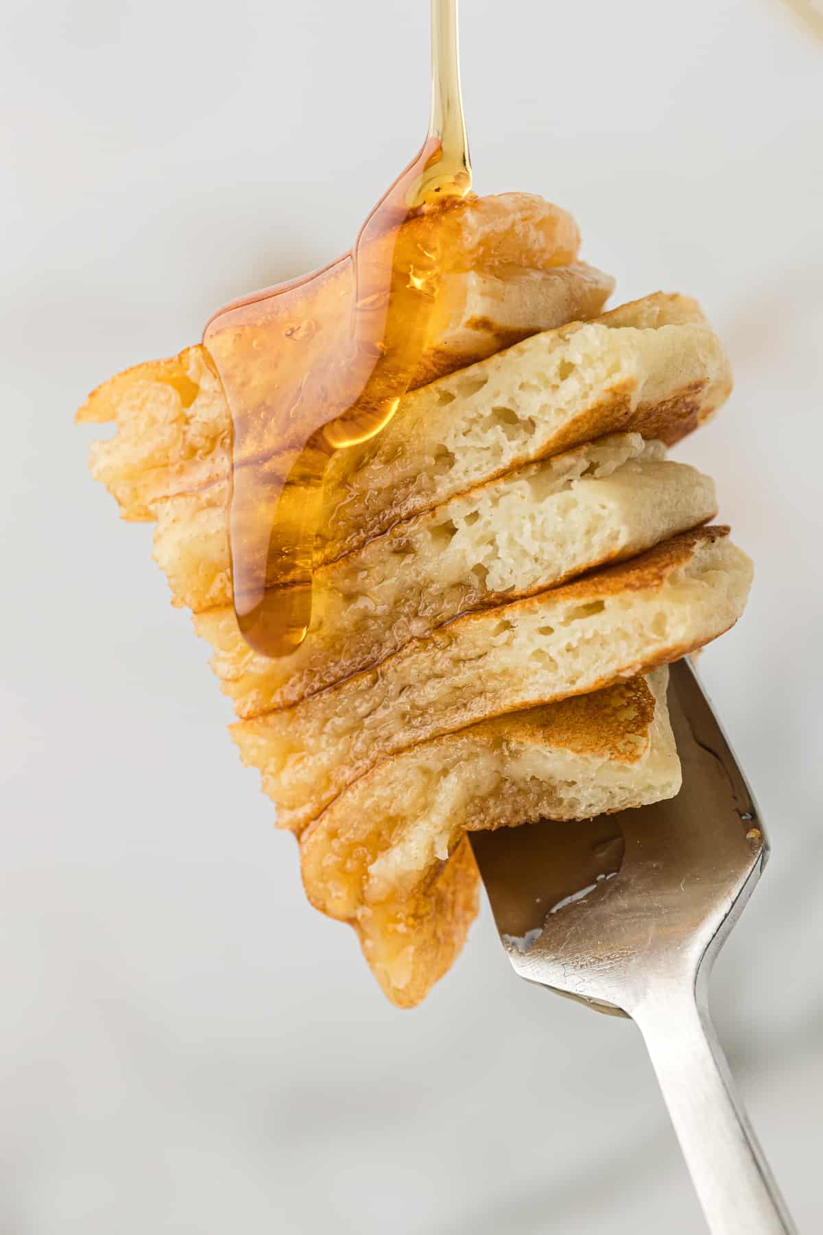 a fork with 5 bite-sized slices of buttermilk pancake on it being drizzles with syrup
