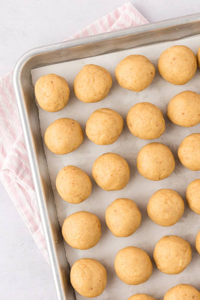 a sheet pan lined with rows of cake pop balls, sitting on top of a white and pink striped towel