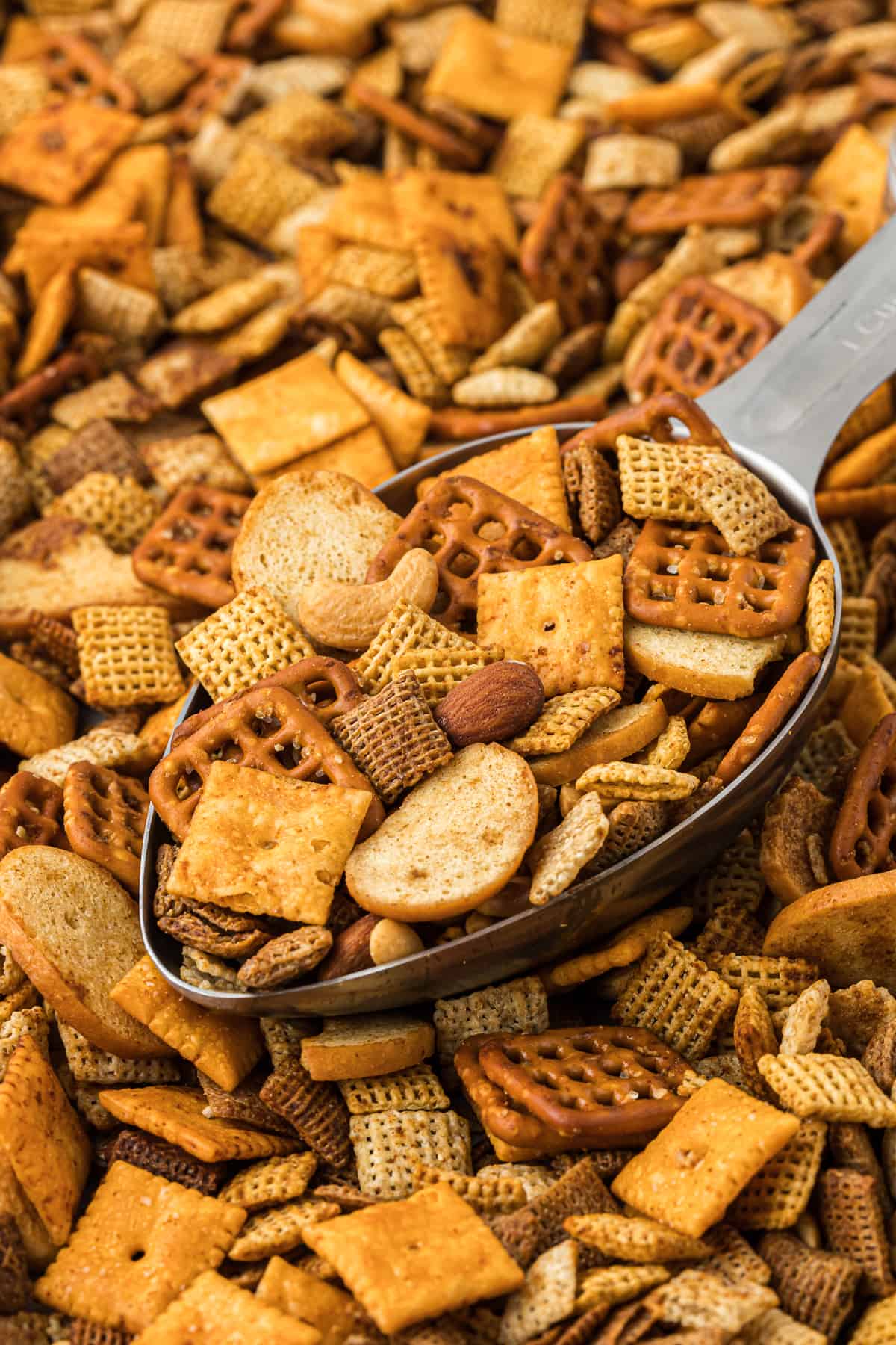 a large metal scoop full of chex mix on top of a bunch more chex mix