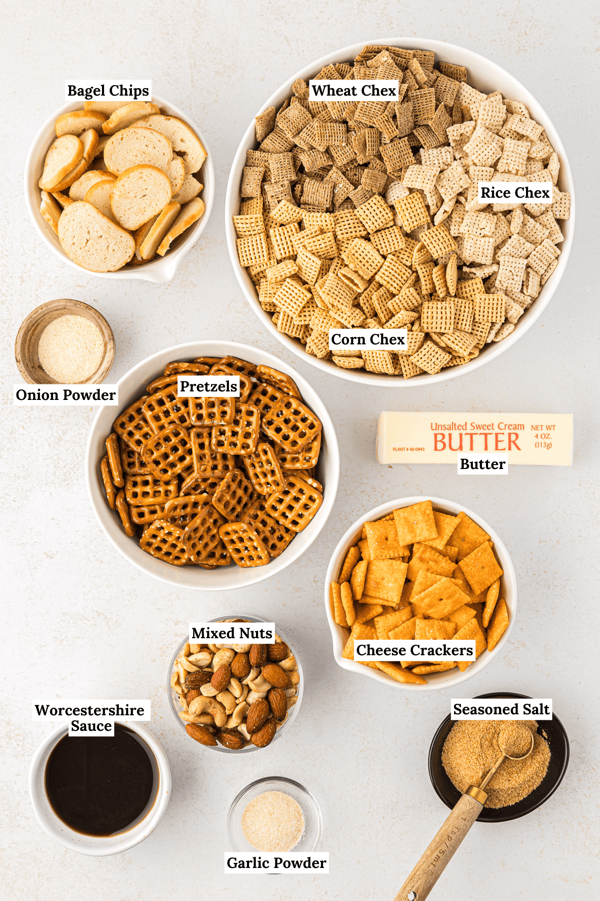over head view of homemade chex mix ingredients including wheat chex, rice chex, corn chex, bagel chips, onion powder, pretzels, a stick of butter, cheese crackers, mixed nuts, seasoned salt, worcestershire sauce, and garlic powder