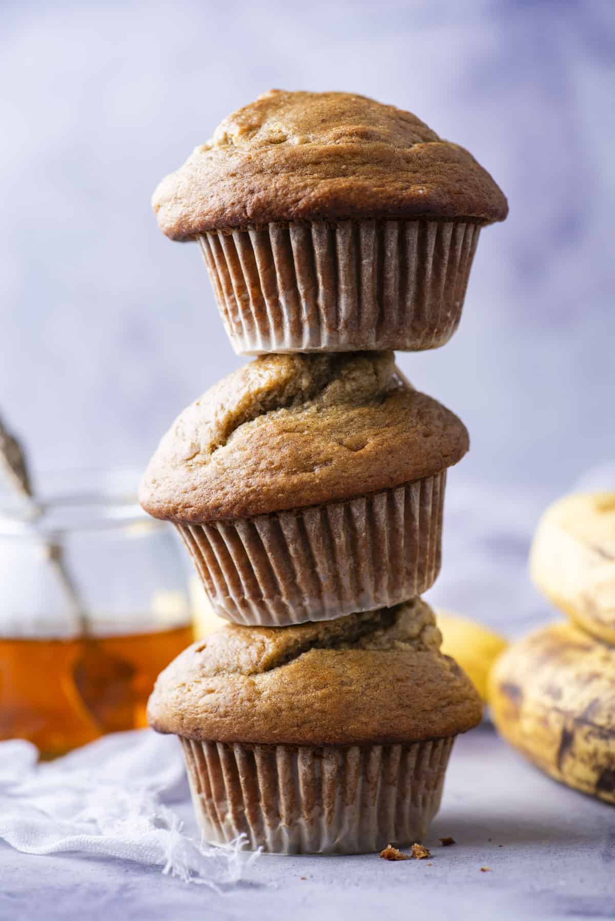 3 healthy banana muffins stacked on top of each other in a tower on purple background