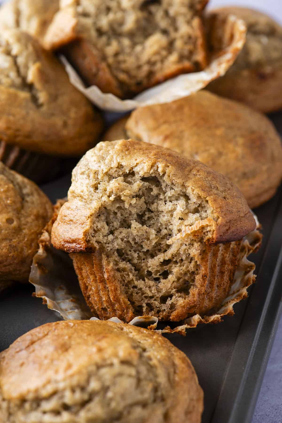 healthy banana muffins arranged in muffin pan with bite removed from center muffin