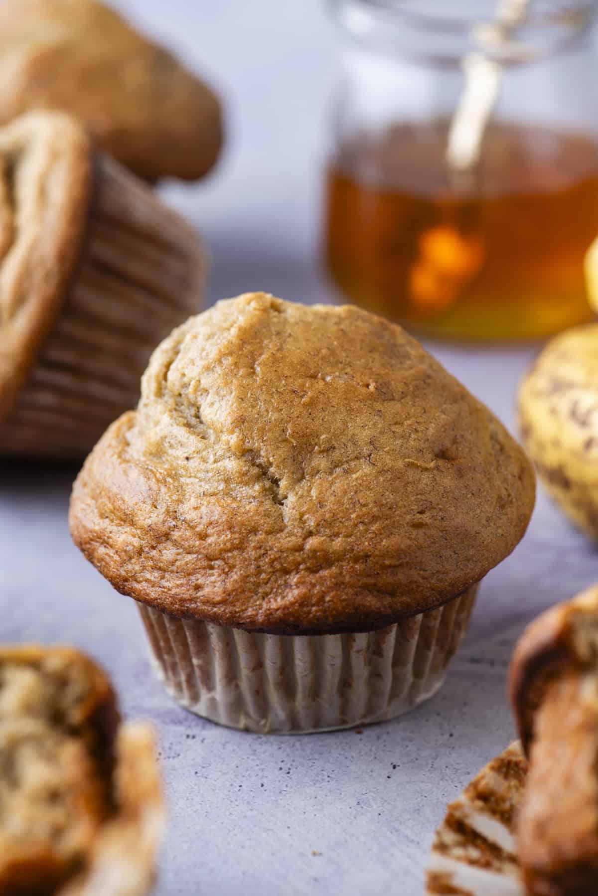 healthy banana muffins on purple background with a jar of honey and bananas in the background 