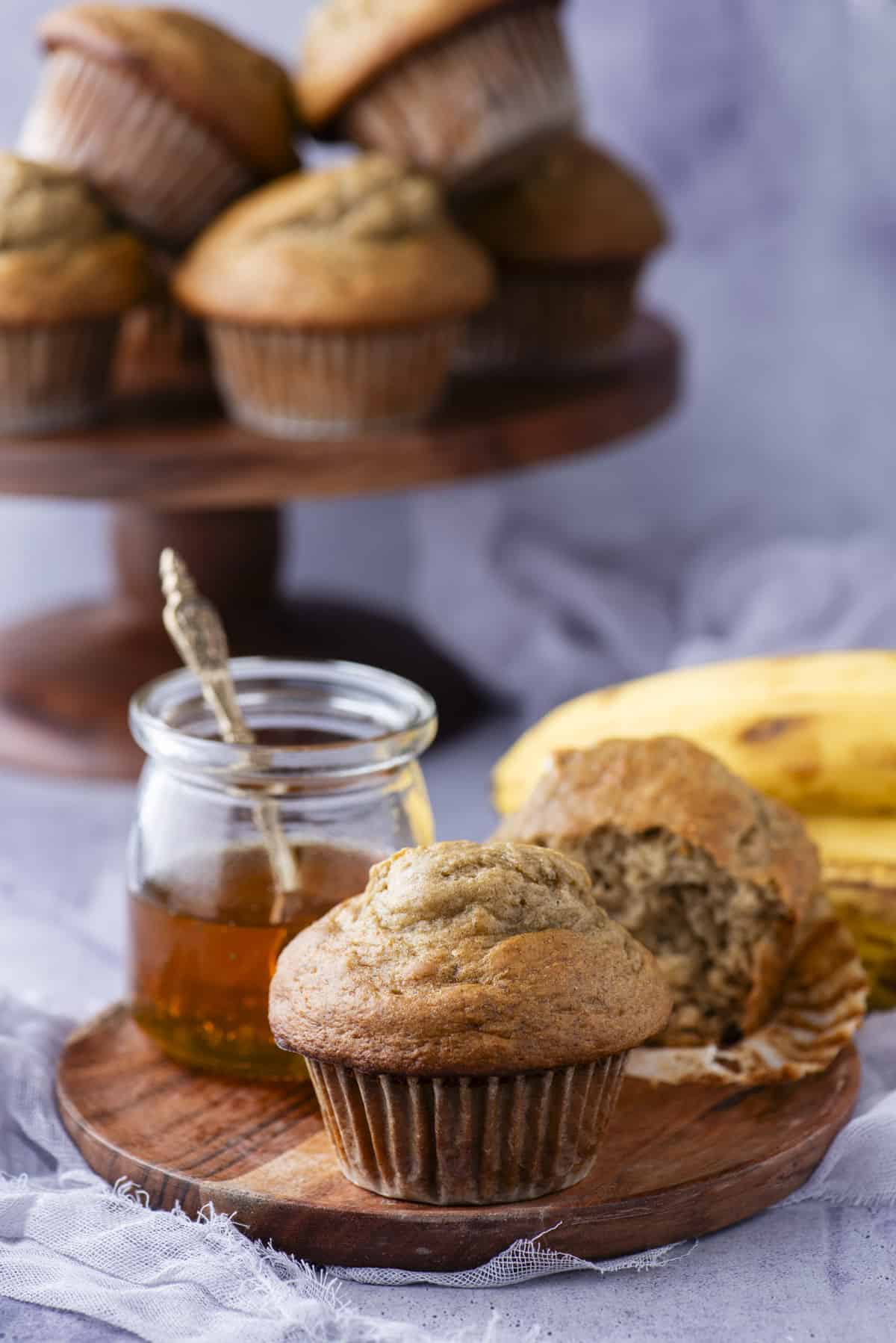 healthy banana muffins on wooden plate with a jar of honey and a muffin with a bite removed from it. 