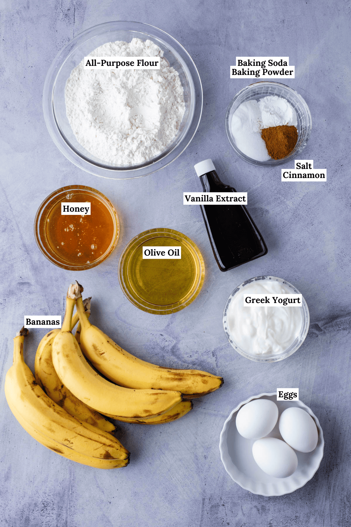 ingredients to make healthy banana muffins arranged on purple background with text overlay