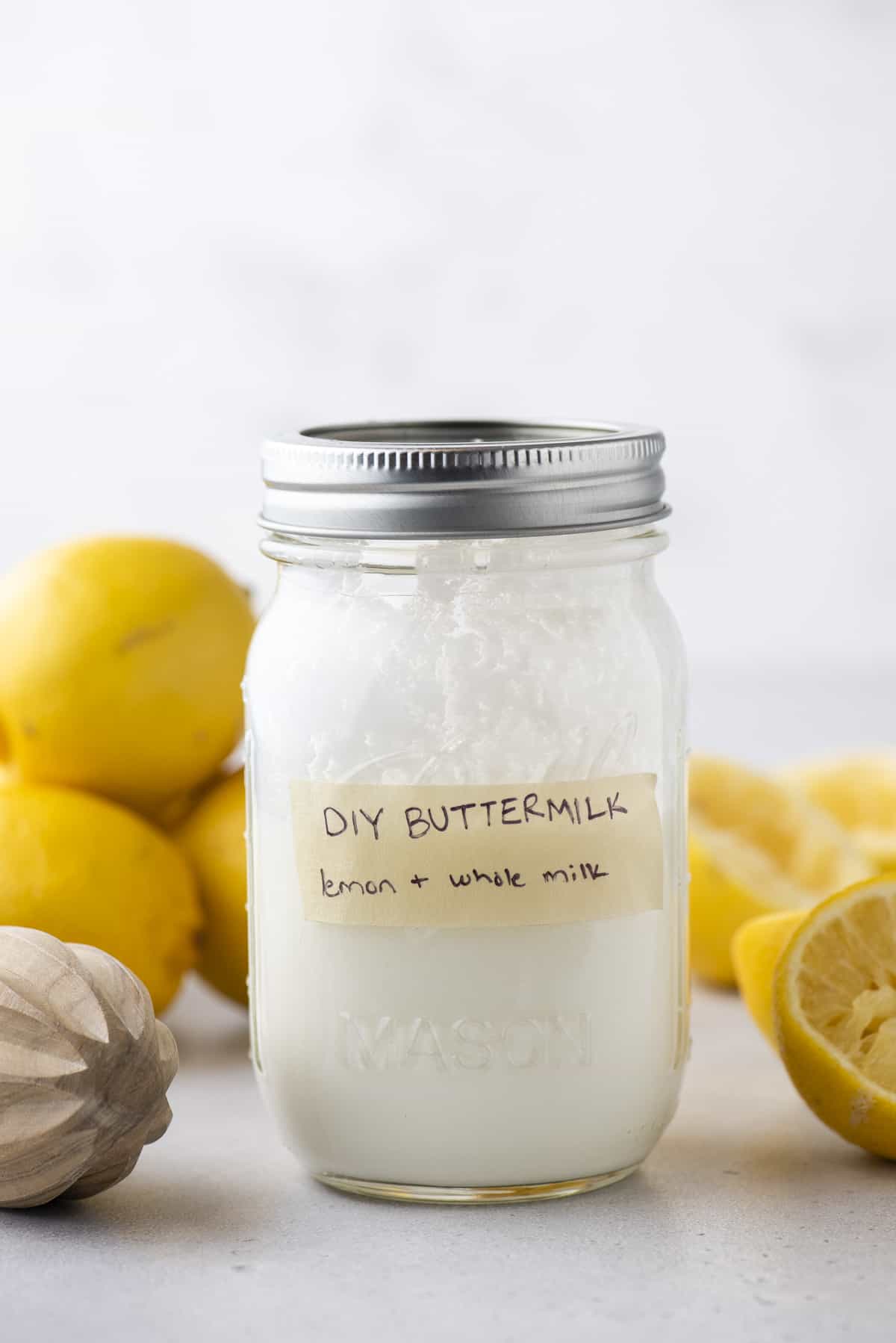 a mason jar full of buttermilk with a strip of tape on it labeled "DIY Buttermilk: lemon + whole milk", with fresh lemons all around