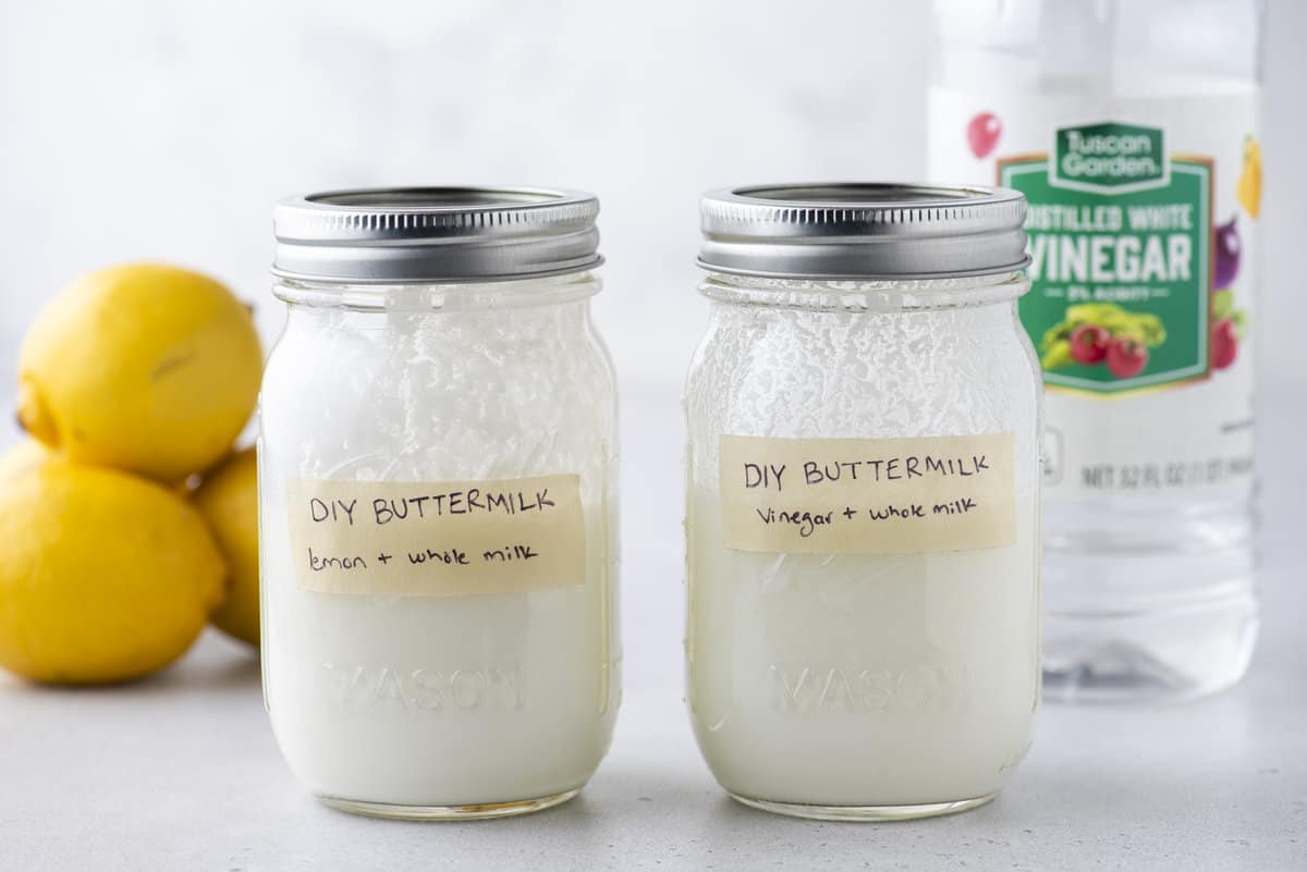 two mason jars with lids on labeled DIY buttermilk with tape with whole fresh lemons and a bottle of distilled vinegar in the background