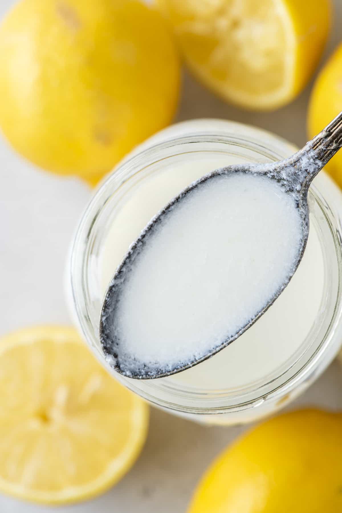 A spoon full of buttermilk being held above a mason jar full of buttermilk with fresh whole and sliced lemons all around