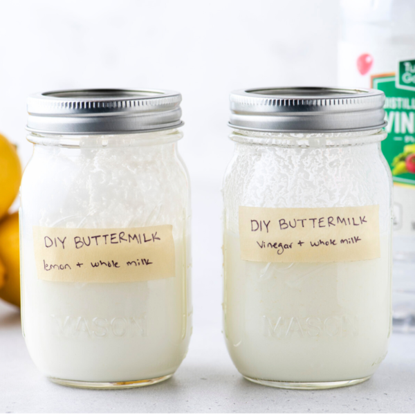 two mason jars with lids on labeled DIY buttermilk with tape with whole fresh lemons and a bottle of distilled vinegar in the background