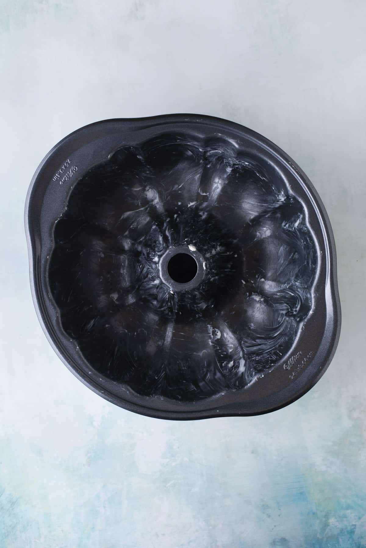 over head view of a greased bundt cake pan sitting on a light blue surface