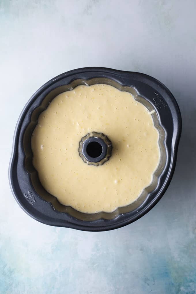 over head view of lemon bundt cake batter inside a bundt pan sitting on a light blue surface