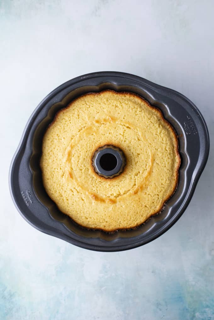 over head view of a lemon bundt cake in the bundt pan sitting on a light blue surface