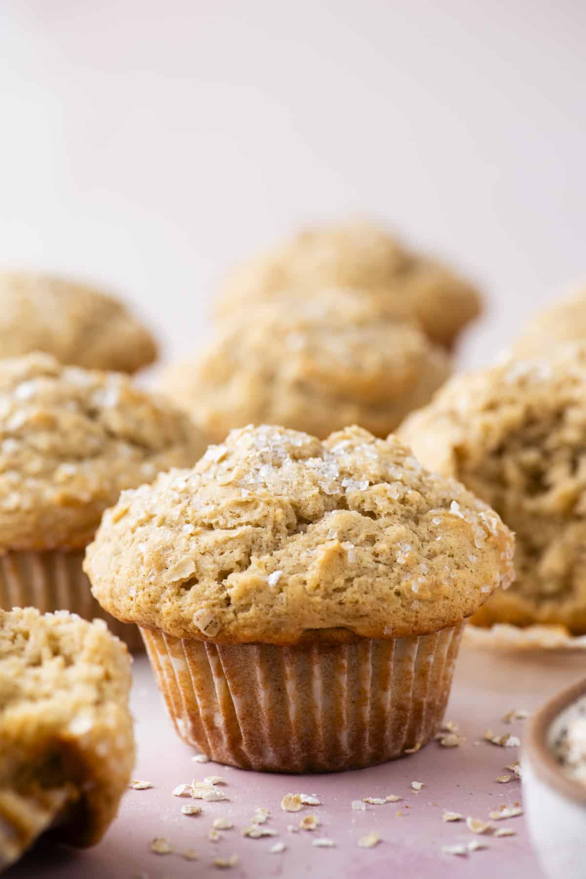 oatmeal muffins on a light pink surface with oats sprinkled around