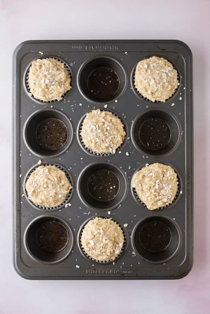 over head view of a muffin pan with oatmeal muffin batter in every other muffin hole