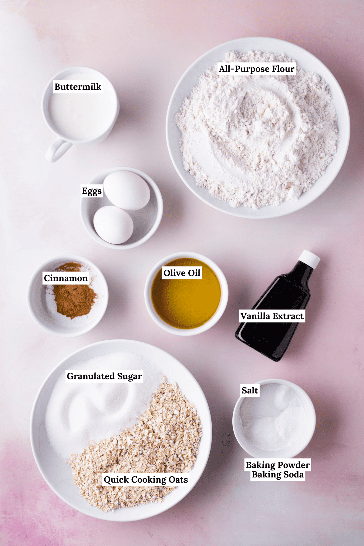 overhead view of the ingredients for oatmeal muffins including buttermilk, all-purpose flour, eggs, cinnamon, olive oil, vanilla extract, granulated sugar, quick cooking oats, salt, baking powder and baking soda