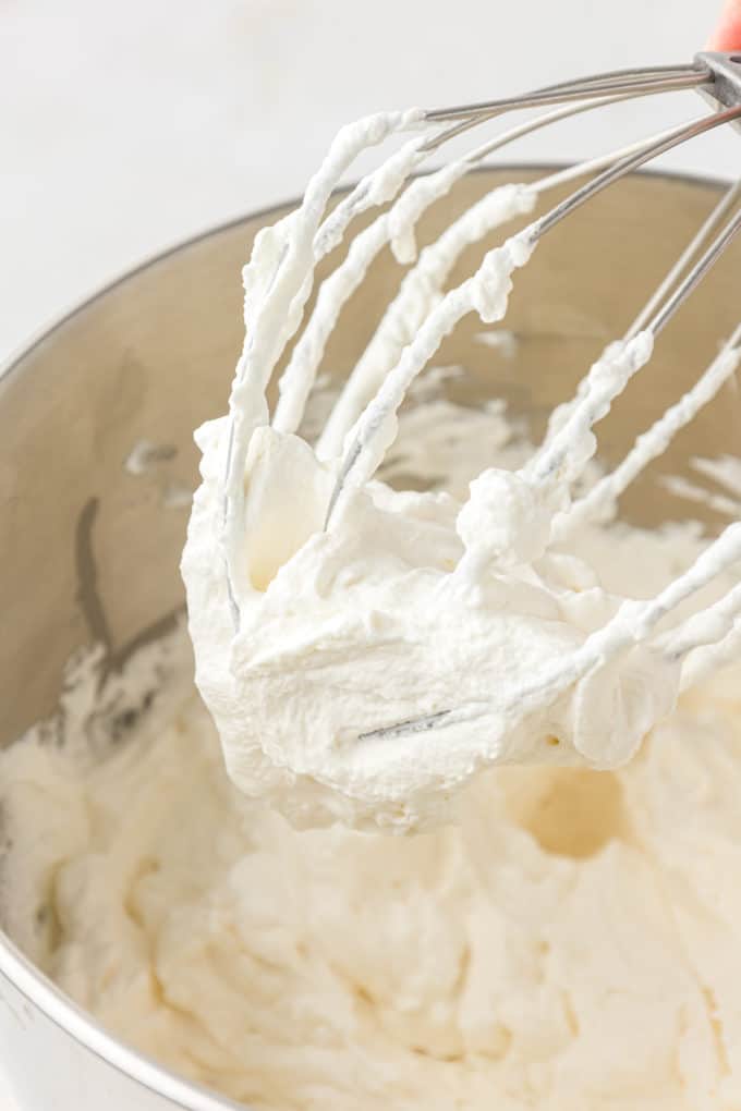 fresh whipped egg whites in a mixing bowl with the mixer lifted and covered in whipped egg whites