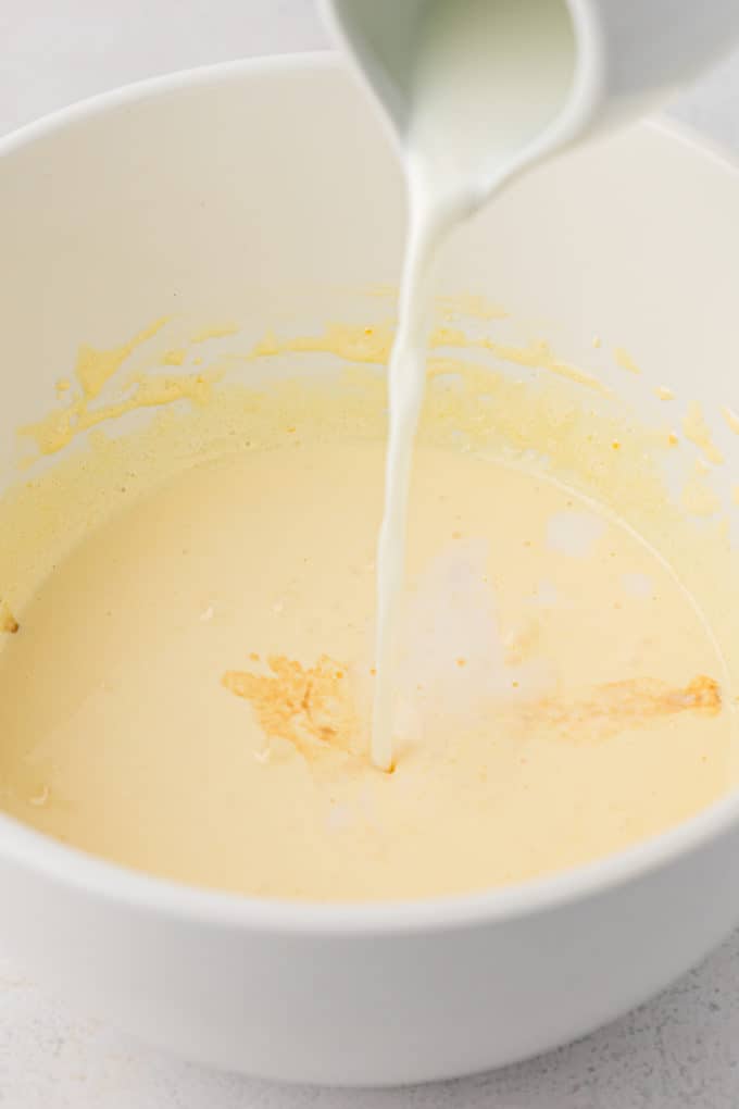 milk being added to a white bowl with an egg and sugar mixture in it