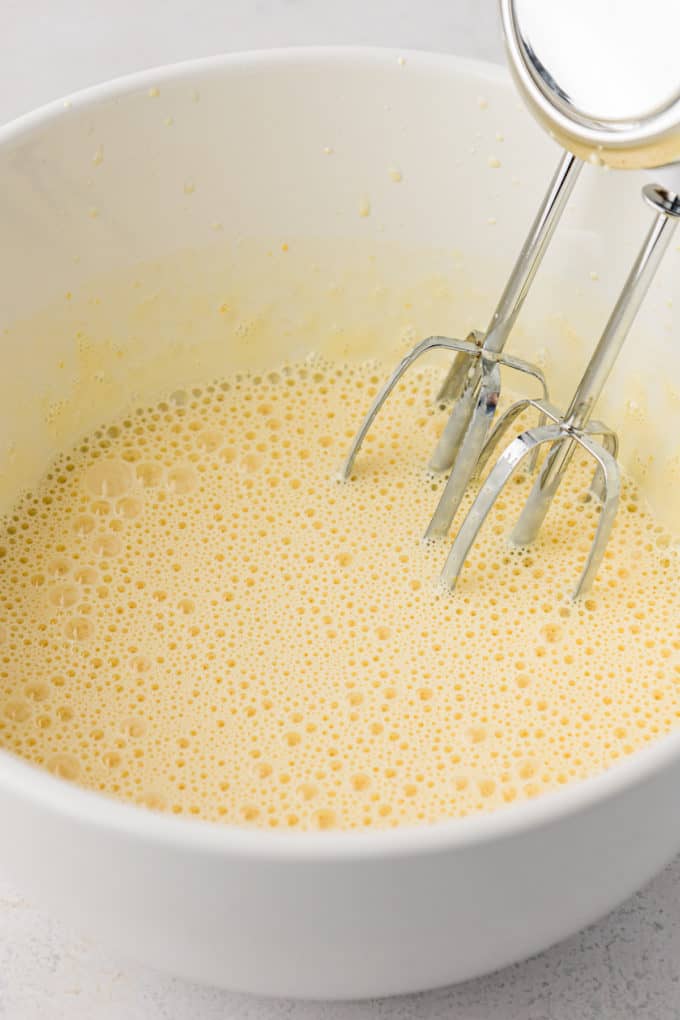 egg and sugar being mixed in a white bowl with an electric mixer