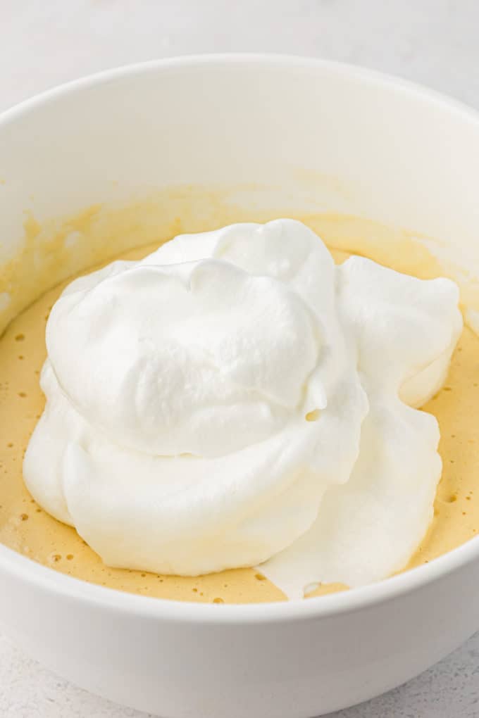 whipped egg whites on top of a white bowl full of cake batter