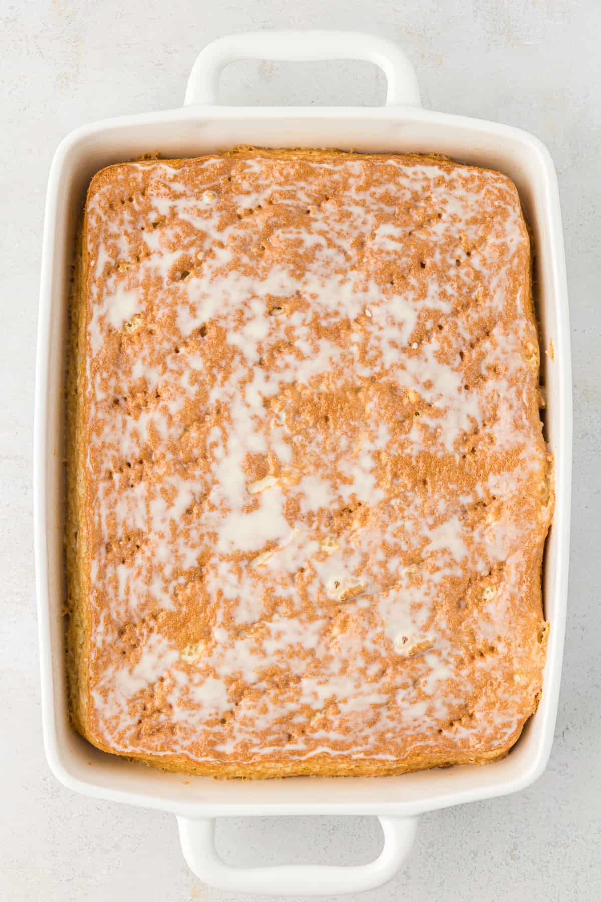 overhead view of a cake in a white rectangular baking dish that has a milk mixture poured over top and soaking into it