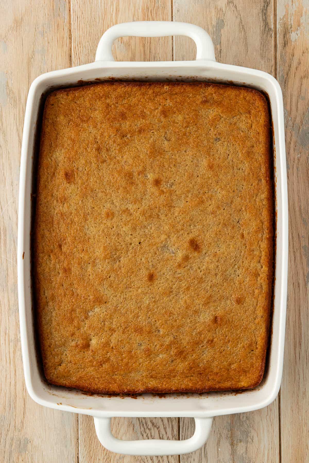 freshly baked banana cake in a 9x13 white dish sitting on a wood surface