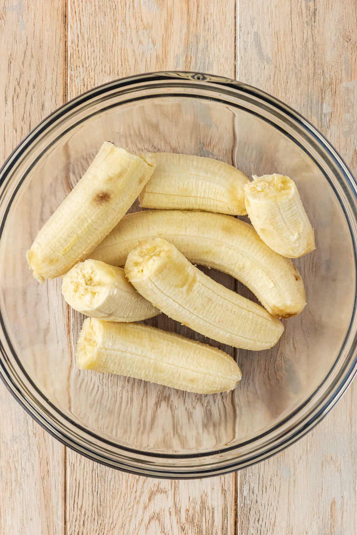 a glass bowl full of banana halves on a wood surface