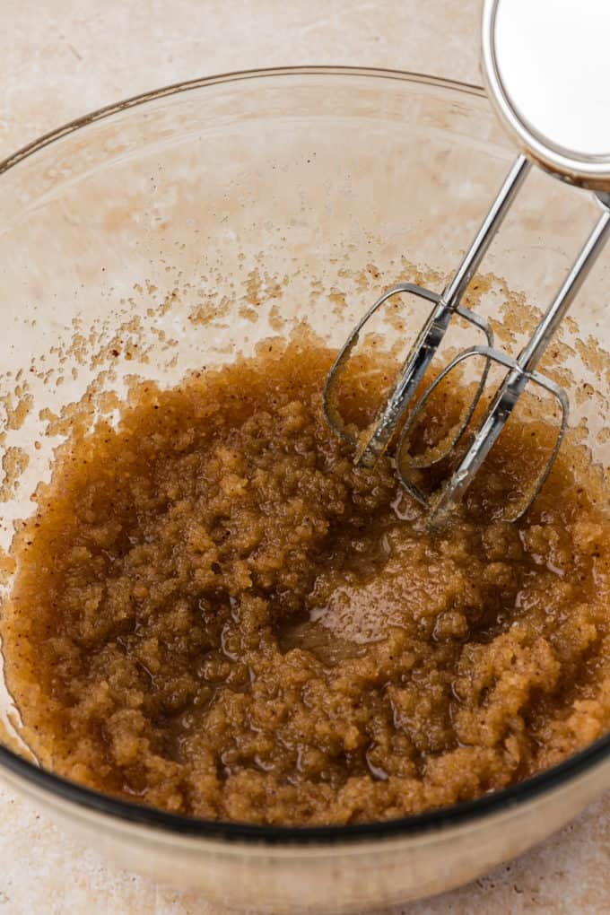 brown sugar, granulated sugar and butter being mixed in a clear glass bowl with an electric mixer