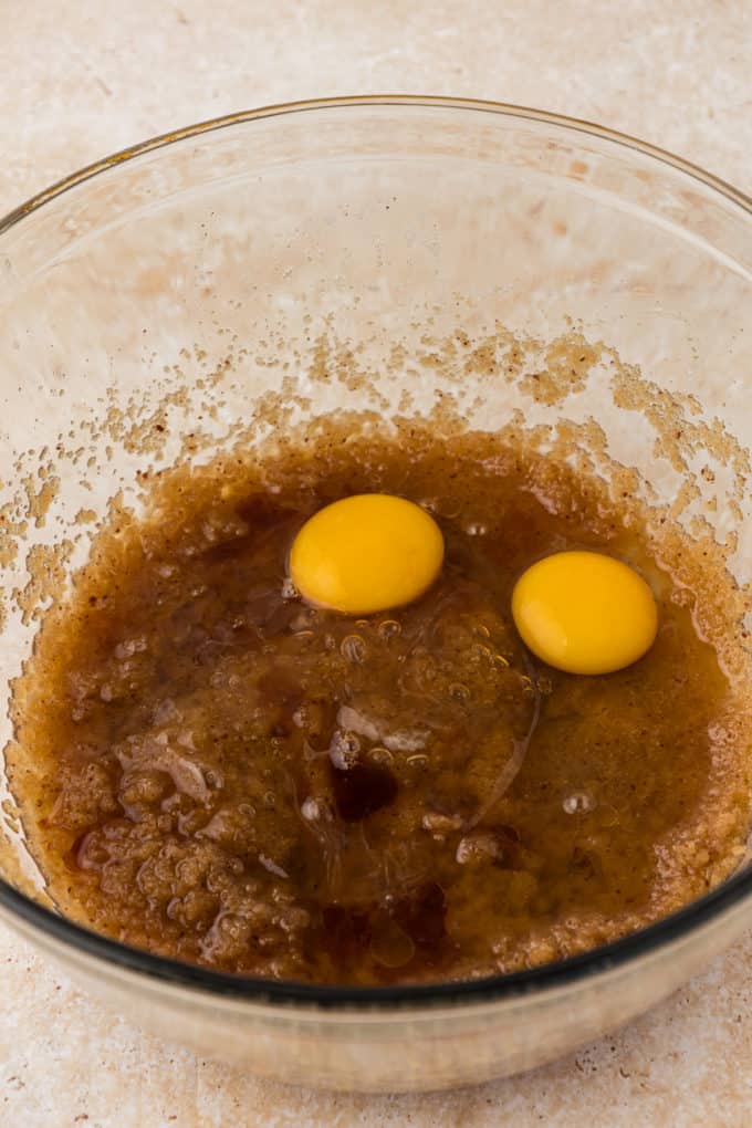 butter and brown sugar mixture in a clear glass bowl with two eggs on top that have not been mixed in yet