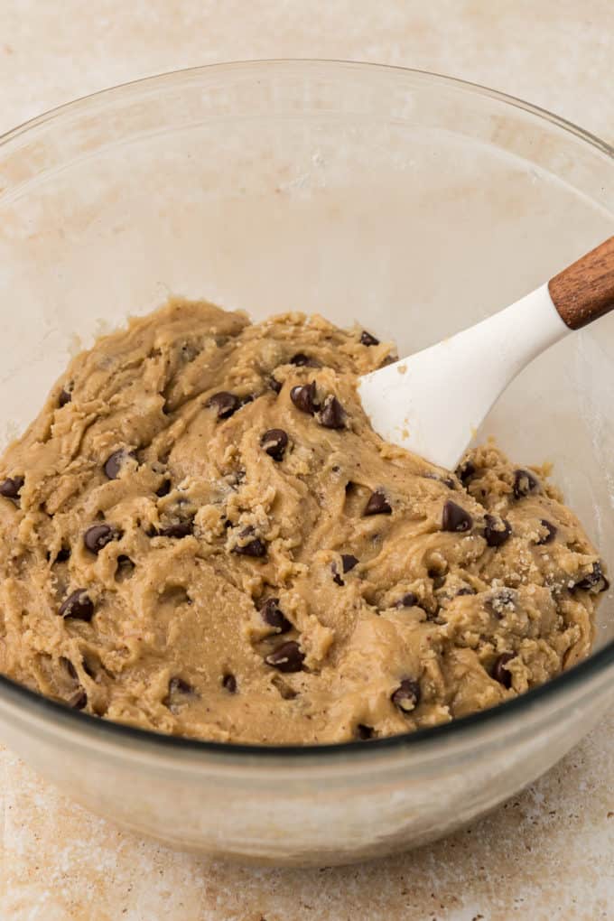 a white spatula in a clear glass bowl full of chocolate chip cookie dough