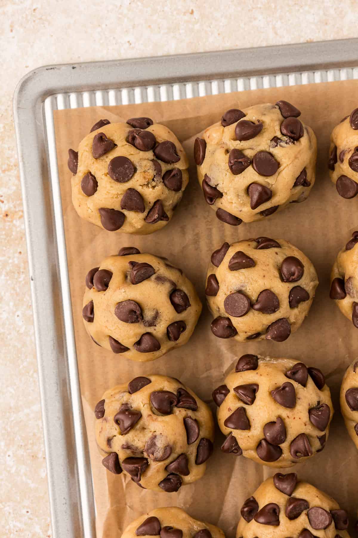 rows of chocolate chip cookie dough balls on a baking sheet lined with parchment paper