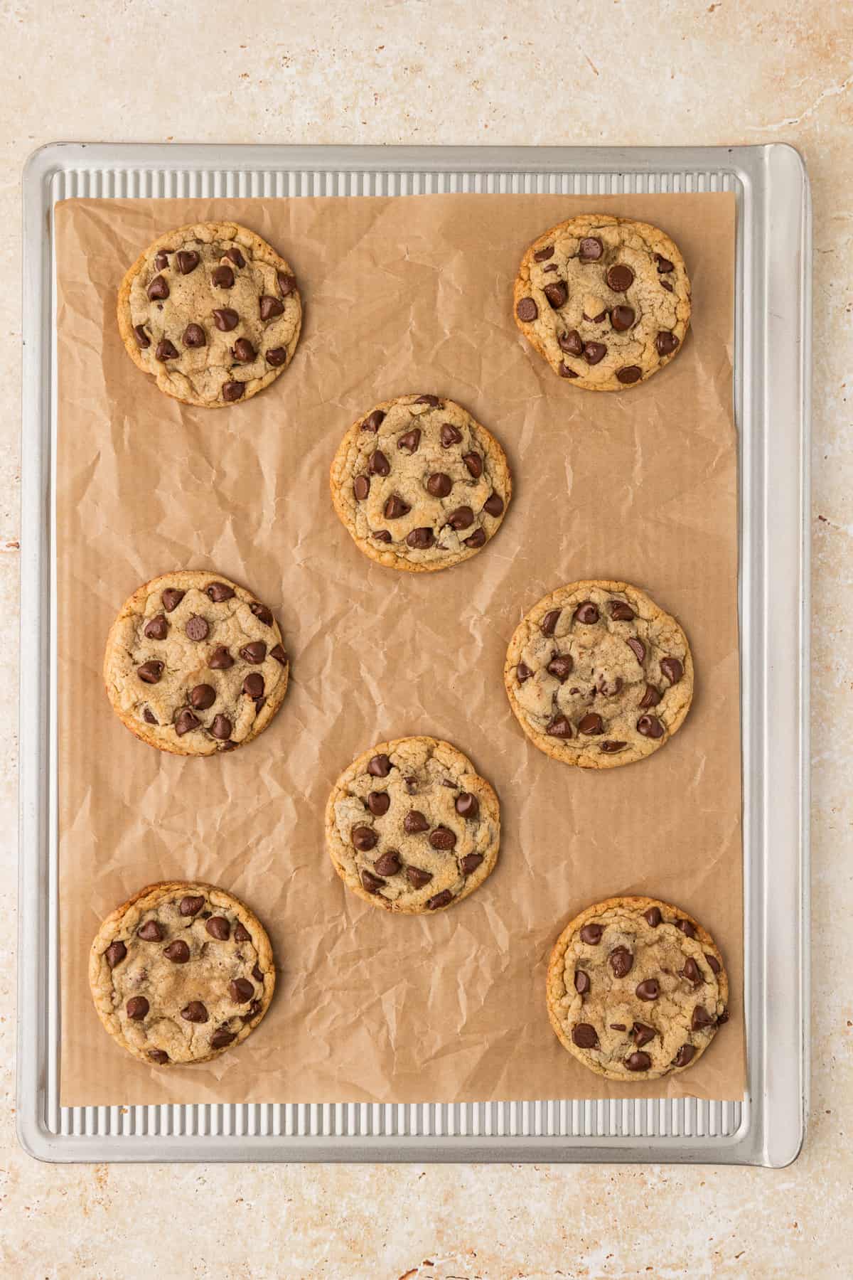 over head view of a cookie sheet lined with parchment paper with brown butter chocolate chip cookies spaced out over the pan