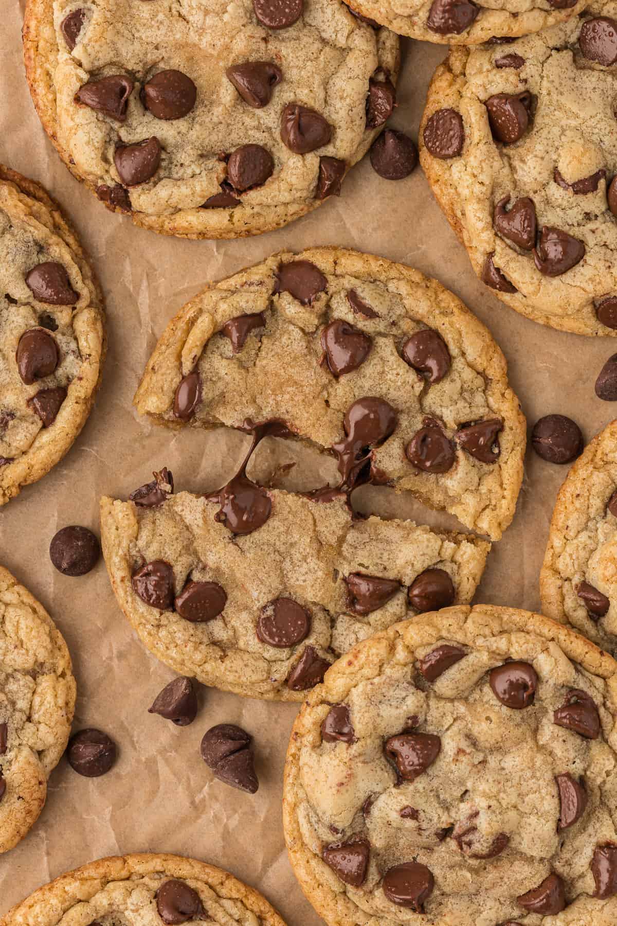 over head view of brown butter chocolate chip cookies on parchment paper with the middle cookie pulled apart at the middle and chocolate chips scattered around