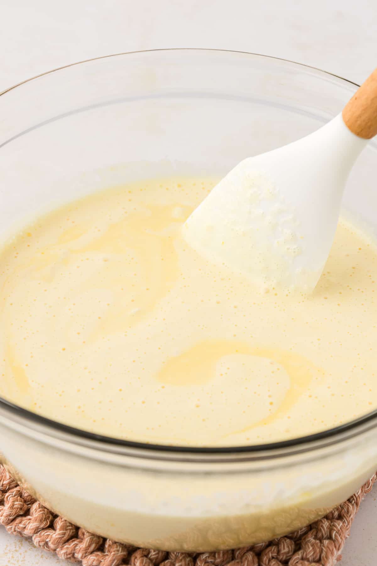 a cream mixture for creme brulee being mixed in a clear glass bowl with a white spatula
