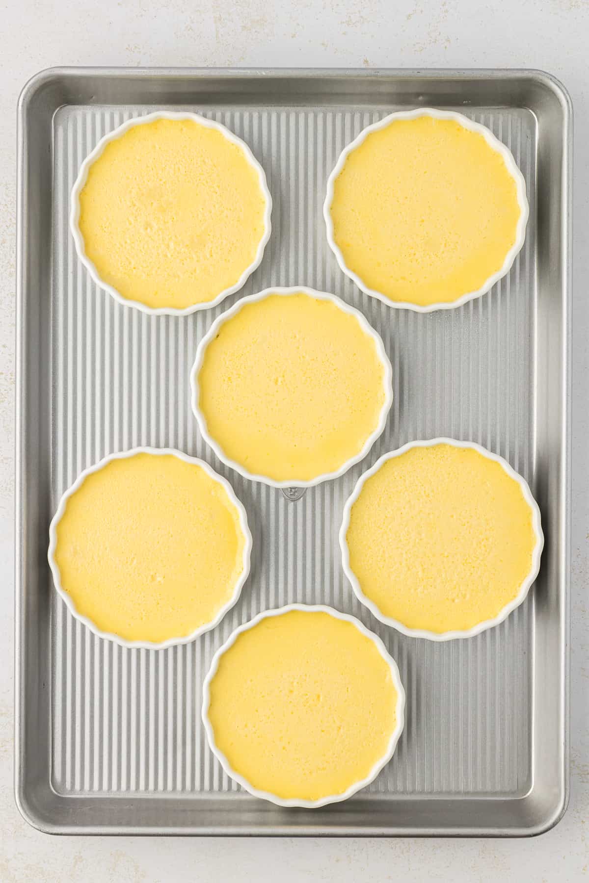 over head view of a baking sheet with 6 white ramekins of freshly baked creme brulee on it
