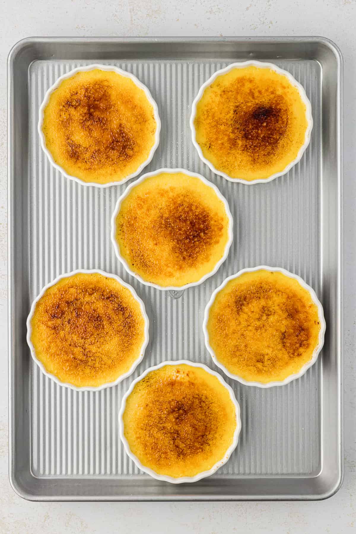 a baking sheet with six ramekins of creme brulee with caramelized tops on it